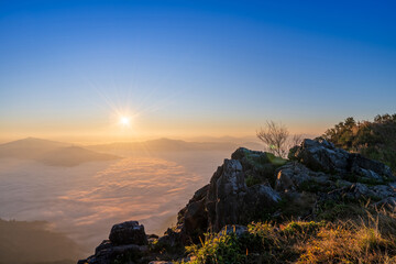 Sun rising above mist with rocks in the foreground and mountain view.