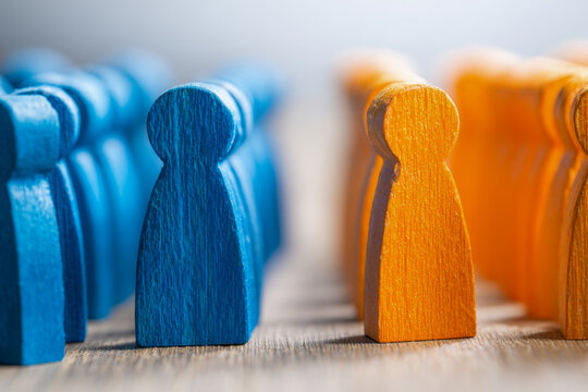 Meeting of two opposing groups represented by blue and orange wooden figures facing each other in a conceptual team or negotiation setting on a wooden surface