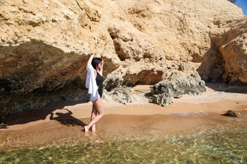 woman black swimsuit and a white shirt runs along the beach, a summer vacation concept by the sea.