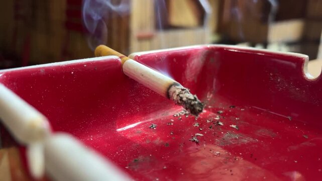 a lit cigarette on a red ashtray