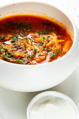 A bowl of hearty, vibrant red soup garnished with fresh herbs and served with sour cream on an elegant white platter atop a modern granite countertop