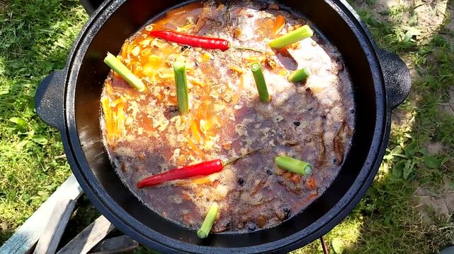 Pilaf cooking in cast iron cauldron outdoors bubbling broth and spices