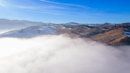 Aerial photography of a mountain plateau in winter season. Photography was taken from a drone at a higher altitude, above the clouds with a curvy road under. 