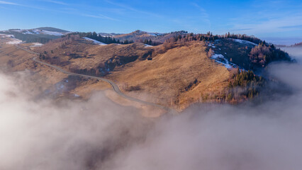 Aerial photography of a mountain plateau in winter season. Photography was taken from a drone at a higher altitude, above the clouds with a curvy road under. 