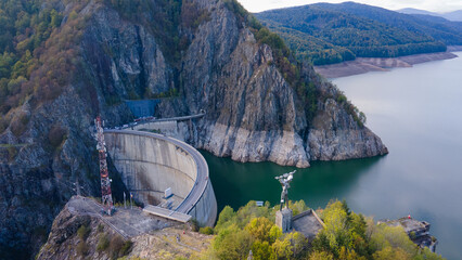 Aerial photography of Vidraru dam, in Romania. Photography was shot from a drone from the right side of Vidraru dam with the dam and the lake in the view and mountains in the background.