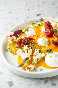 Vibrant, elegant plated appetizer of yellow beet or persimmon carpaccio topped with figs, cheese, microgreens, and popcorn on a modern gray background