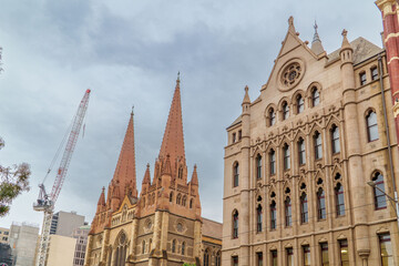 Gothic Revival Architecture Dominates Melbourne's Cityscape, Featuring a Historic Cathedral and Ornate Building Under a Cloudy Sky.