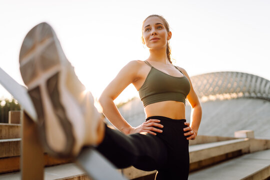 A young woman in sportswear exercises outdoors in the sun. Athlete performs a stretching exercise on special platform. Concept: sports, recreation. Active lifestyle. - Powered by Adobe