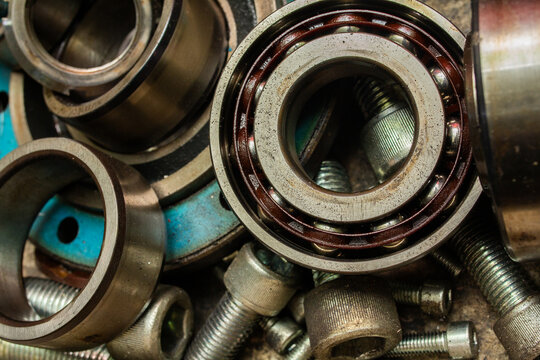 Various steel ball bearings, sleeves, bolts, and industrial fasteners covered in oil residue, illustrating machinery disassembly for servicing and mechanical repair