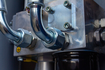 Shiny chrome hydraulic/pneumatic pipe fittings and steel bolts attached to a heavy, machined metallic manifold block, emphasizing fluid power systems and industrial quality