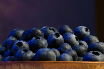 A close-up view of fresh blueberries in a wooden bowl with blue backlight.