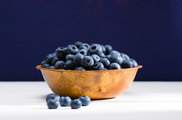 Fresh Blueberries in a wooden bowl on a white wooden table 