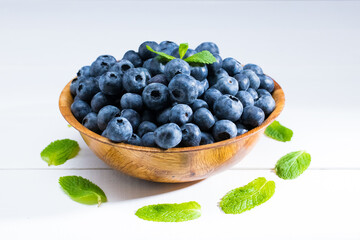 Fresh Blueberries with mint leaves in a wooden bowl on a white wooden table .