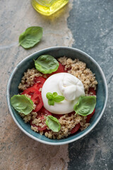 Green bowl with quinoa, burrata cheese and tomatoes, vertical shot on a grey and beige stone background, high angle view