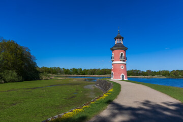 Moritzburg Lighthouse on the Castle Pond in bright sunlight. Path with shadow running past the lighthouse and its brick facade. History and tourism