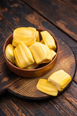 Sweet, golden jackfruit pods (bulbs) in a wooden bowl on a rustic dark wood table. Tropical fruit snack with copy space. © Mironov