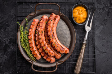Grilled and cut sausages (frankfurters/wieners) on a rustic platter with mustard sauce and thyme on a dark textured background.