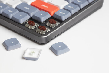Close-up of mechanical keyboard with removed keycaps revealing brown switches and scattered arrow keys on white surface
