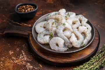 Raw peeled shrimp prawn in a cast iron skillet on a dark rustic wood background. Overhead shot with copy space and spices.