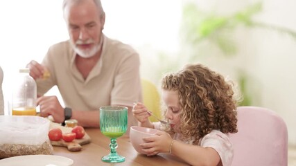 Happy grandfather and cute curly-haired granddaughter enjoying a nutritious morning meal. The family shares a bonding moment over breakfast - Powered by Adobe