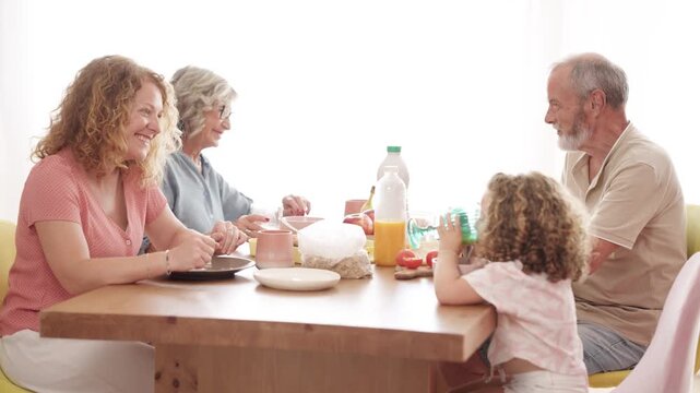 Cheerful three-generation family enjoying a healthy breakfast at home. Grandparents, mother, and a little girl sharing a happy moment