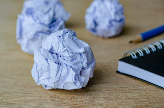 A closeup view of crumpled sheets of paper resting near a spiral notebook and pencil.