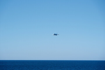 White Commercial Passenger Airplane Flying Over Sea in Clear Blue Sky