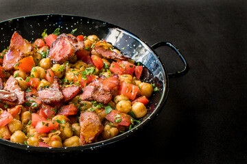 Rustic Mediterranean Chickpeas and Smoked Meat Stew with Diced Tomatoes and Parsley in a Black Skillet