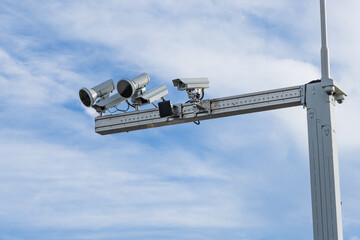 High-tech traffic enforcement cameras mounted on a gantry for speed control and phone usage detection against a blue sky.
