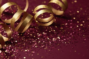 Golden ribbons and glitter on a dark red surface close up view shot