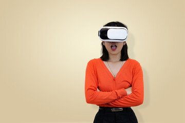 Calm and confident young Asian woman in an orange sweater wearing a virtual reality headset, standing with crossed arms, symbolizing intense focus and control