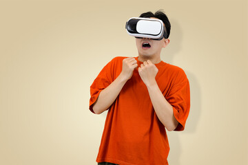 Shocked or scared young Asian man in an orange t-shirt wearing a VR headset, with an open mouth and clenched hands, reacting intensely to a frightening or surprising moment in the virtual world
