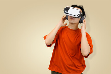 Excited young Asian man in an orange t-shirt wearing a virtual reality headset, symbolizing immersive entertainment or controlling the sound of the metaverse in studio background