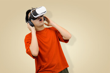 Excited young Asian man in an orange t-shirt wearing a virtual reality headset, symbolizing immersive entertainment or controlling the sound of the metaverse in studio background