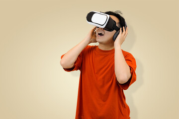 Excited young Asian man in an orange t-shirt wearing a virtual reality headset, symbolizing immersive entertainment or controlling the sound of the metaverse in studio background