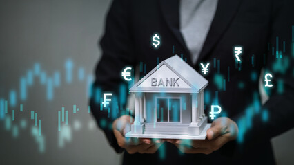 Business person holding bank model with glowing international currency exchange symbols.