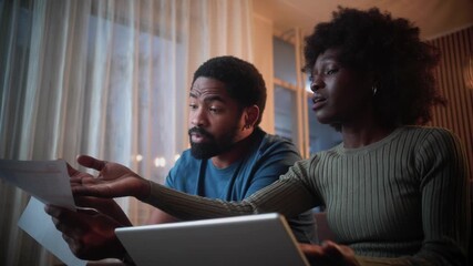 Black couple checking bank documents using laptop at home. Young man and woman reading paper bills, calculating expenses or taxes, planning future finances, doing paperwork. - Powered by Adobe