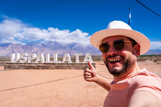 Hombre turista con sombrero tom&aacute;ndose una selfie frente al cartel de la ciudad de Uspallata, en Mendoza