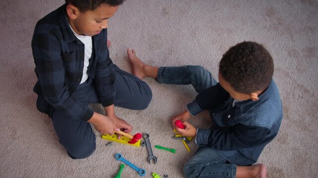 Top view two little African American boys play with toys ethnic siblings friends kids children sons playing game on carpet at home holding hammer screwdriver spanner family adoption custody hobby fun