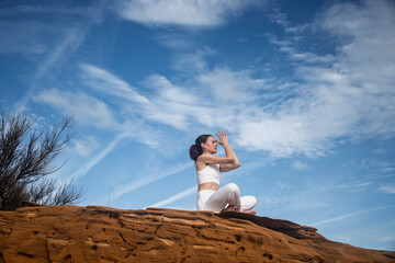 woman sitting on a red rock meditating and practicing yoga