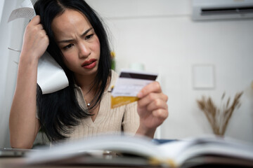 An Asian woman sits indoors holding receipts and a credit card, appearing concerned. The scene...