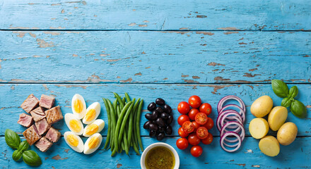 Fresh Ni&ccedil;oise salad ingredients laid out on a distressed blue wooden background, overhead view.