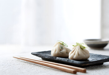 close-up view of two delicate dumplings arranged on black slate plate with fresh green onions in the center of quiet white room, showing why this simple chinese dish.