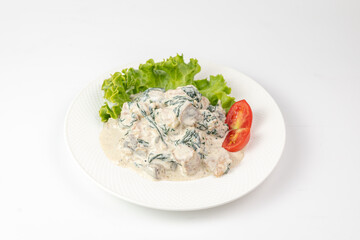 Close-up of chicken in creamy sauce with spinach and mushrooms on white background - appetizing dish