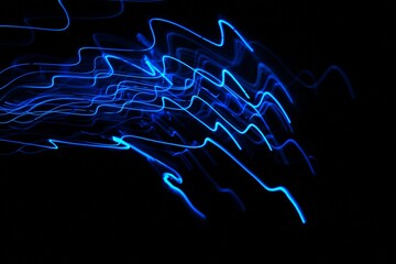 Long exposure light painting photography. Jagged swirls of electric blue light against a black background