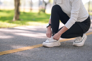 Adult Asian woman ties athletic shoes on a park path preparing for a fitness activity healthy...
