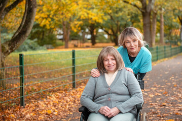 Elderly woman with grey hair in wheelchair on a walk in the park in fall weather with nurse or...