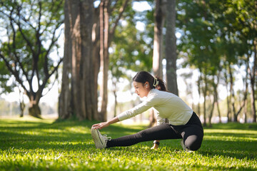 Fototapeta premium Asian adult woman stretches exercise for health wellness body flexibility workout in tranquil sunny green park nature fitness journey