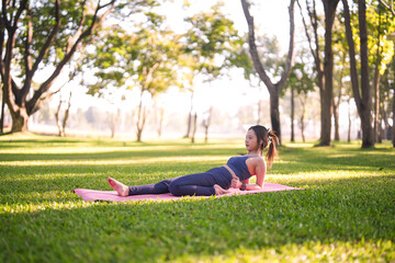 Asian adult woman performs yoga stretching exercise on pink mat in peaceful green park promoting wellness and healthy lifestyle fitness outdoors