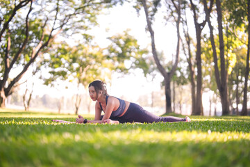 Young Asian woman performing outdoor yoga stretch in sunny park practicing healthy wellness fitness lifestyle mindful movement exercise